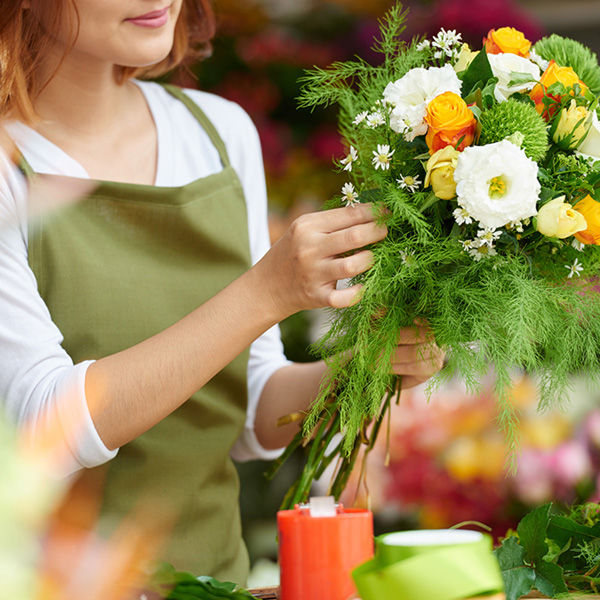 Eine Floristin bindet einen wunderschönen Blumenstrauß mit weißen, gelben und orangen Blüten. So ein schönes Geschenk!