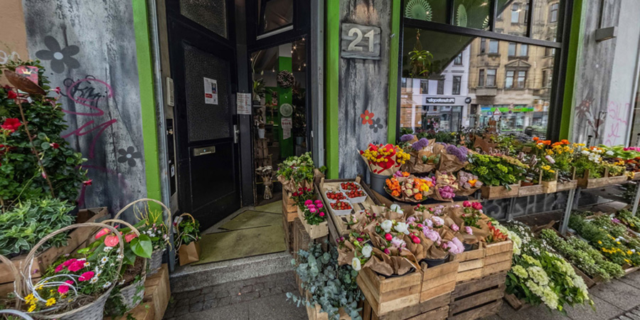 Fassade eines Blumenladens mit verschiedenen Blumen und Pflanzen in Körben und Kisten vor dem Eingang.