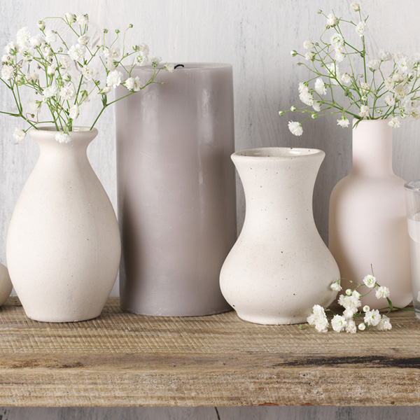 Gemütliches Deko-Arrangement: Zarte Blumen in Keramikvasen und eine graue Kerze auf einem Holzbord. Perfekt für ein entspanntes Ambiente!